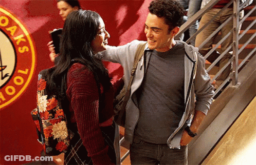 A Man And A Woman Are Standing Next To Each Other In Front Of A Sign That Says Oak 'S School GIF