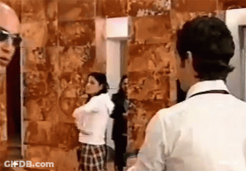 A Man And A Woman Are Standing Next To Each Other In Front Of A Wall Covered In Pictures . GIF