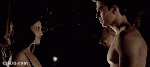 A Man And A Woman Are Standing Next To Each Other In The Dark Looking At Each Other . GIF