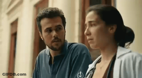 A Man And A Woman Are Standing Next To Each Other Looking At Each Other . GIF
