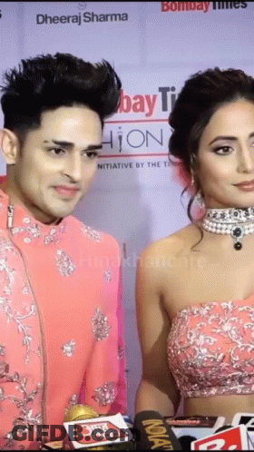 A Man And A Woman Are Standing Next To Each Other On A Red Carpet In Front Of A Sign That Says Bombay Times GIF