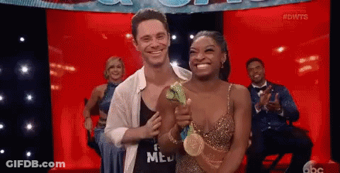 A Man And A Woman Are Standing Next To Each Other On A Stage Holding A Gold Medal . GIF