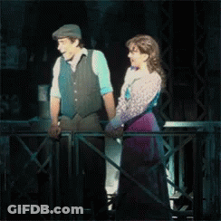 A Man And A Woman Are Standing Next To Each Other On A Stage . GIF