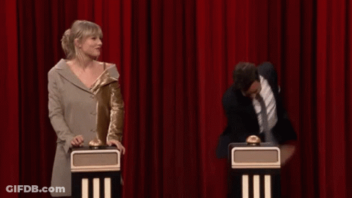 A Man And A Woman Are Standing Next To Each Other On A Stage With A Red Curtain Behind Them . GIF