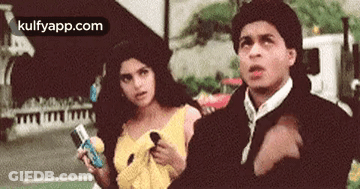 A Man And A Woman Are Standing Next To Each Other On A Street . The Man Is Pointing At The Woman . GIF