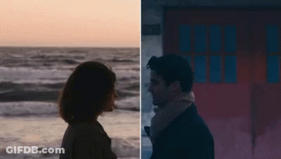 A Man And A Woman Are Standing Next To Each Other On The Beach And Looking At Each Other . GIF