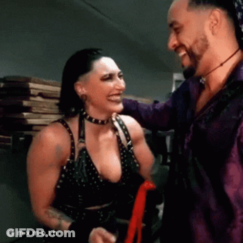 A Man And A Woman Are Standing Next To Each Other Smiling And Laughing . GIF