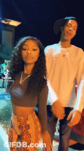 A Man And A Woman Are Standing Next To Each Other . The Woman Is Wearing A Crop Top And Pants . GIF