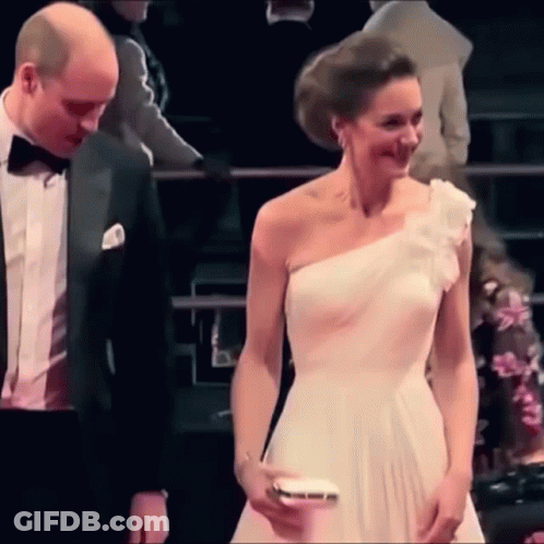 A Man And A Woman Are Standing Next To Each Other . The Woman Is Wearing A White One Shoulder Dress . GIF
