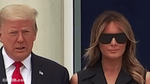 A Man And A Woman Are Standing Next To Each Other Wearing Sunglasses . GIF