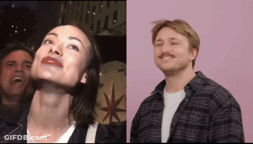 A Man And A Woman Are Standing Next To Each Other With A Sign That Says Hollywood In The Background GIF