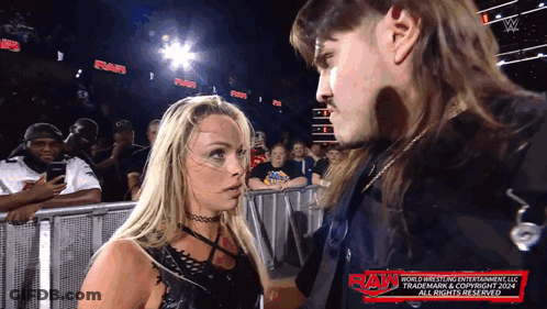 A Man And A Woman Are Standing Next To Each Other With The Word Raw On The Bottom Right GIF