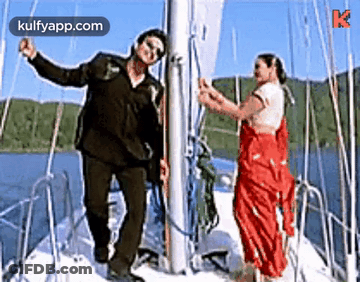 A Man And A Woman Are Standing On A Boat . GIF