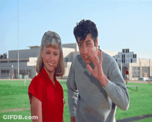 A Man And A Woman Are Standing On A Field And The Man Is Waving GIF