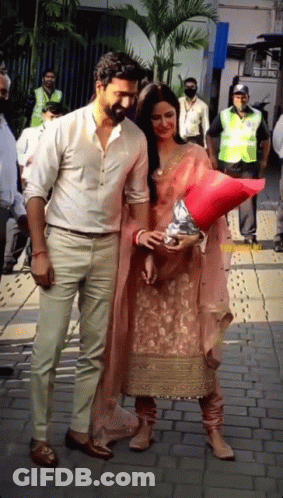 A Man And A Woman Are Standing On A Sidewalk Holding Hands GIF