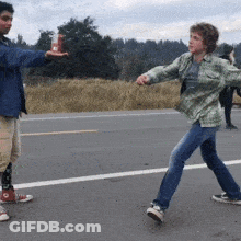 A Man And A Woman Are Standing On The Side Of A Road GIF