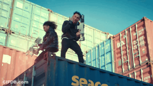 A Man And A Woman Are Standing On Top Of A Seaco Shipping Container GIF