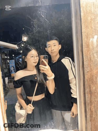 A Man And A Woman Are Taking A Picture In A Mirror GIF