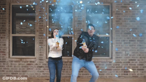 A Man And A Woman Are Throwing Blue Confetti In Front Of A Brick House GIF