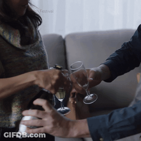 A Man And A Woman Are Toasting With Champagne In Front Of A Film Festival Logo GIF