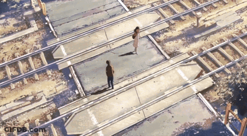 A Man And A Woman Are Walking Across A Train Track GIF