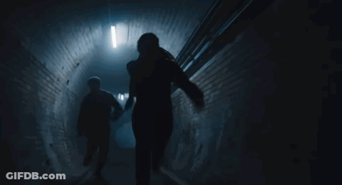 A Man And A Woman Are Walking Down A Dark Tunnel Holding Hands . GIF
