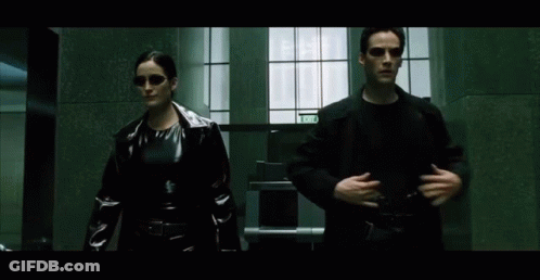 A Man And A Woman Are Walking Down A Hallway With A Sign That Says Exit On It GIF
