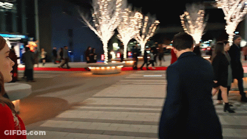 A Man And A Woman Are Walking Down A Sidewalk In Front Of A Sign That Says ' Abercrombie & Fitch ' GIF