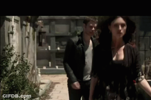 A Man And A Woman Are Walking Down A Sidewalk Next To Each Other . GIF