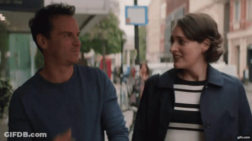 A Man And A Woman Are Walking Down A Street And Looking At Each Other . GIF