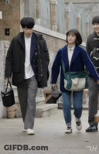 A Man And A Woman Are Walking Down A Street . GIF