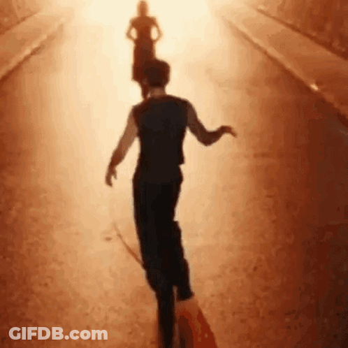 A Man And A Woman Are Walking Down A Street In The Sunlight . GIF