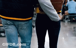 A Man And A Woman Are Walking In A Hallway Holding Hands GIF