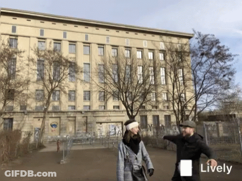 Man And Woman Walking In Front Of Lively Building GIF
