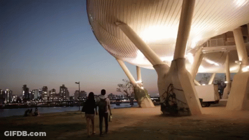 A Man And A Woman Are Walking In Front Of A Building GIF