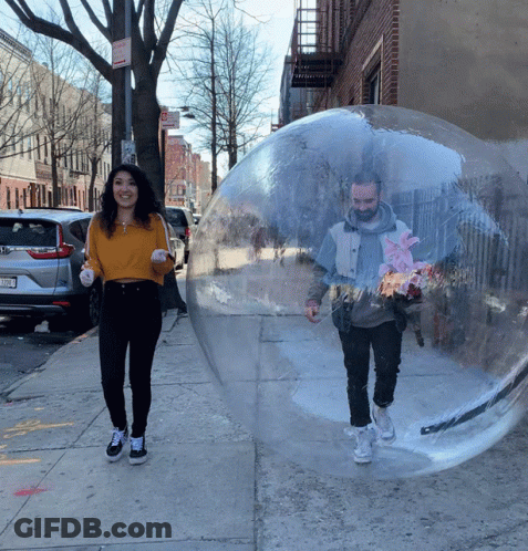 A Man And A Woman Are Walking Through A Clear Bubble On A Sidewalk With A No Parking Sign In The Background GIF
