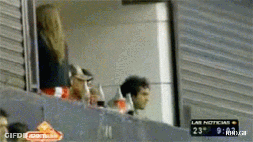 A Man And A Woman Are Watching A Game With A Sign That Says Las Noticias On It GIF