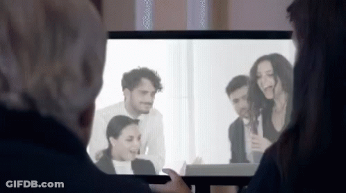 A Man And A Woman Are Watching A Group Of People On A Television Screen . GIF