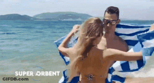 A Man And A Woman Are Wrapped In A Blue And White Striped Towel On A Beach .. GIF