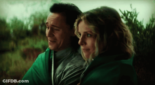 A Man And A Woman Are Wrapped In A Green Blanket And Looking At Each Other . GIF