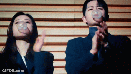 A Man And A Woman Blowing Bubbles In Front Of A Wall GIF