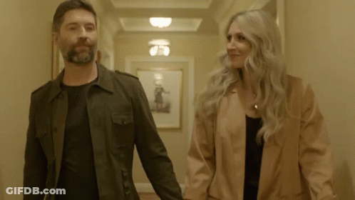 A Man And A Woman Holding Hands In A Hallway GIF