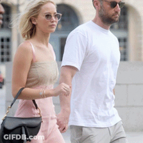 A Man And A Woman Holding Hands While Walking Down A Street GIF