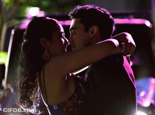 A Man And A Woman Hugging And Kissing In Front Of A Car GIF