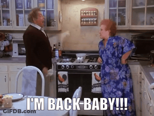 A Man And A Woman In A Kitchen With The Words " I 'M Back Baby " GIF