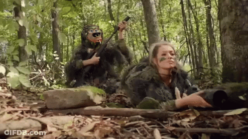 A Man And A Woman In Camouflage Are Laying In The Woods . GIF