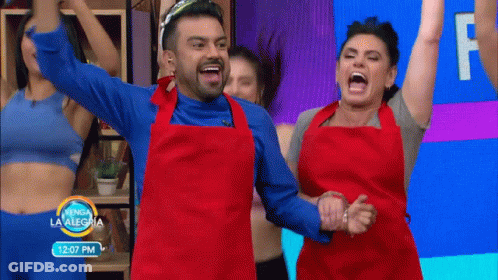 A Man And A Woman In Red Aprons Are Dancing In Front Of A Sign That Says 12:07 Pm GIF