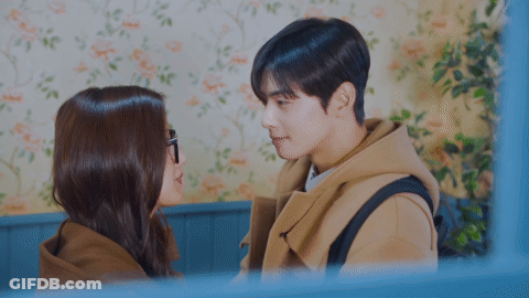 A Man And A Woman Kissing In Front Of A Floral Wall GIF