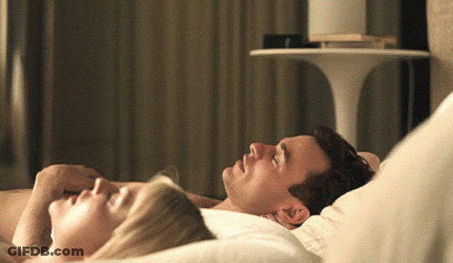 A Man And A Woman Laying On A Bed With Their Eyes Closed GIF