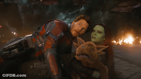A Man And A Woman Looking At Each Other With A Stuffed Animal Between Them GIF